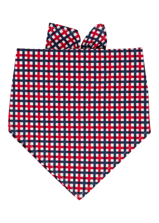 A patriotic themed dog bandana with a red, white, and navy blue plaid pattern, folded into a triangular shape with tie-up ends at the top. 
