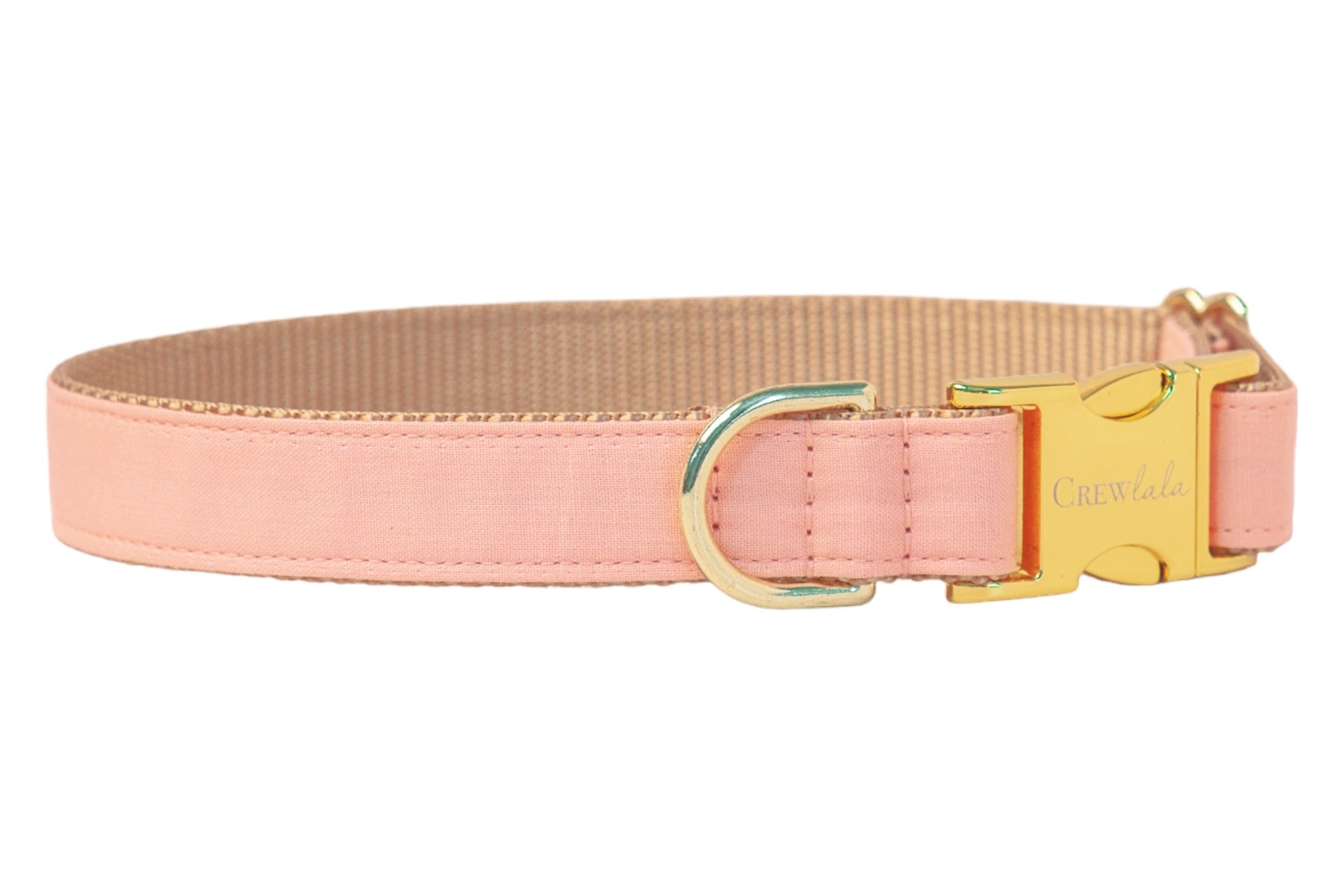 A soft peach pink dog collar with a fabric overlay and tan woven nylon backing. The collar features a polished gold side-release buckle engraved with “Crewlala” and a matching gold D-ring for leash or tag attachment.