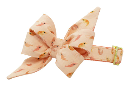 Soft peach dog collar with a fabric bow accent, patterned with warm-toned shrimp and finished with gold metal hardware.