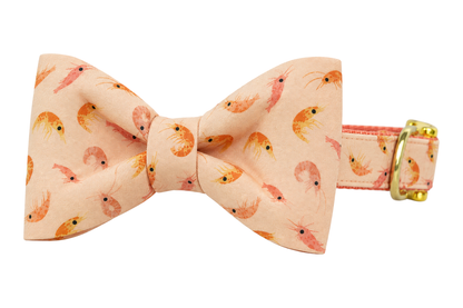Classic dog collar featuring a Peach Prawns fabric bow tie, a soft peach fabric with small coral and pink shrimp, attached to a matching Peach Prawns collar with a nylon inner lining and gleaming gold hardware, including a D-ring and buckle.