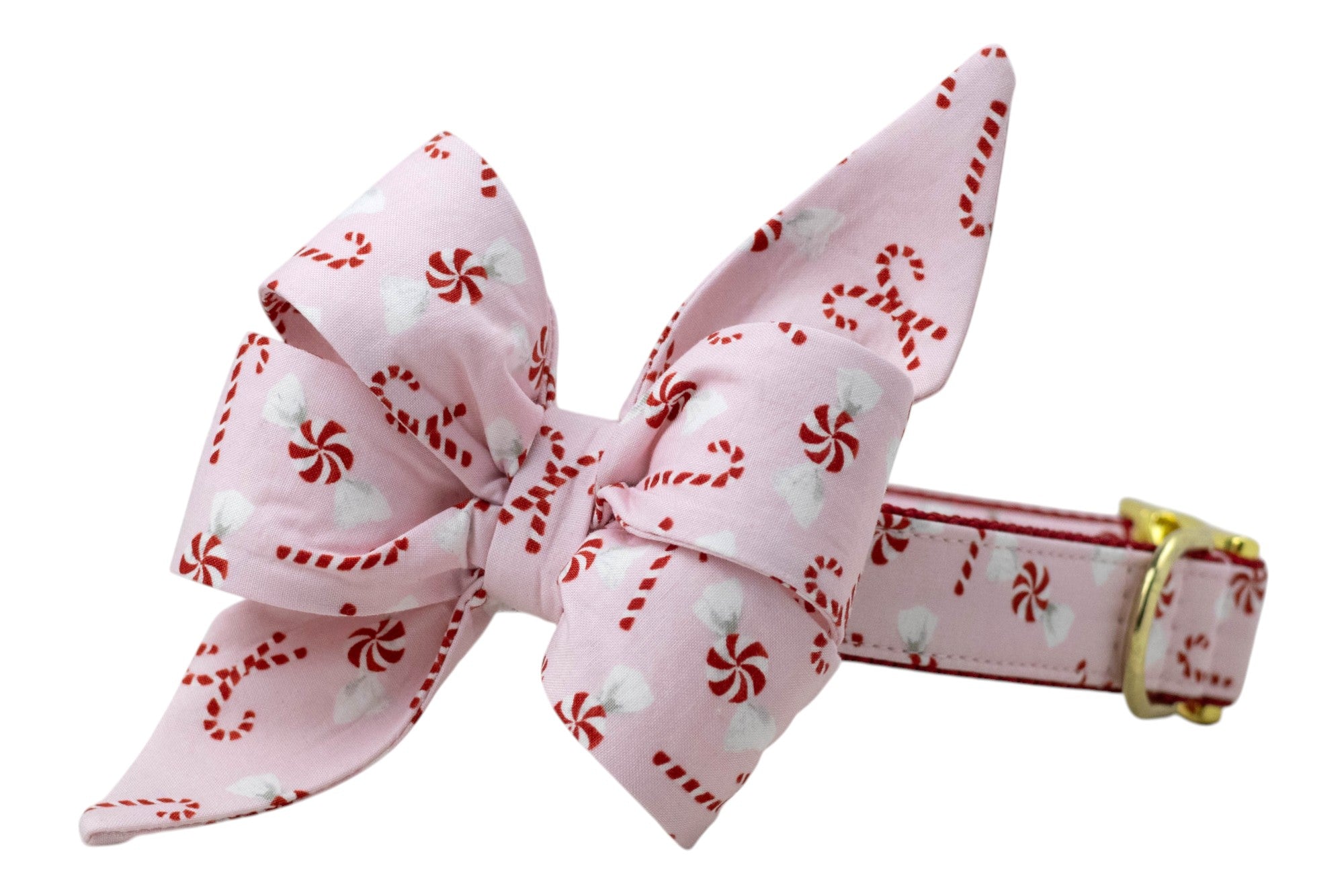 A holiday dog collar with an oversized belle bow attachment, both made from soft pink fabric printed with candy canes and peppermint swirls. The bow features large, structured loops and long pointed tails, while the collar is backed in nylon and finished with polished hardware for festive flair.
