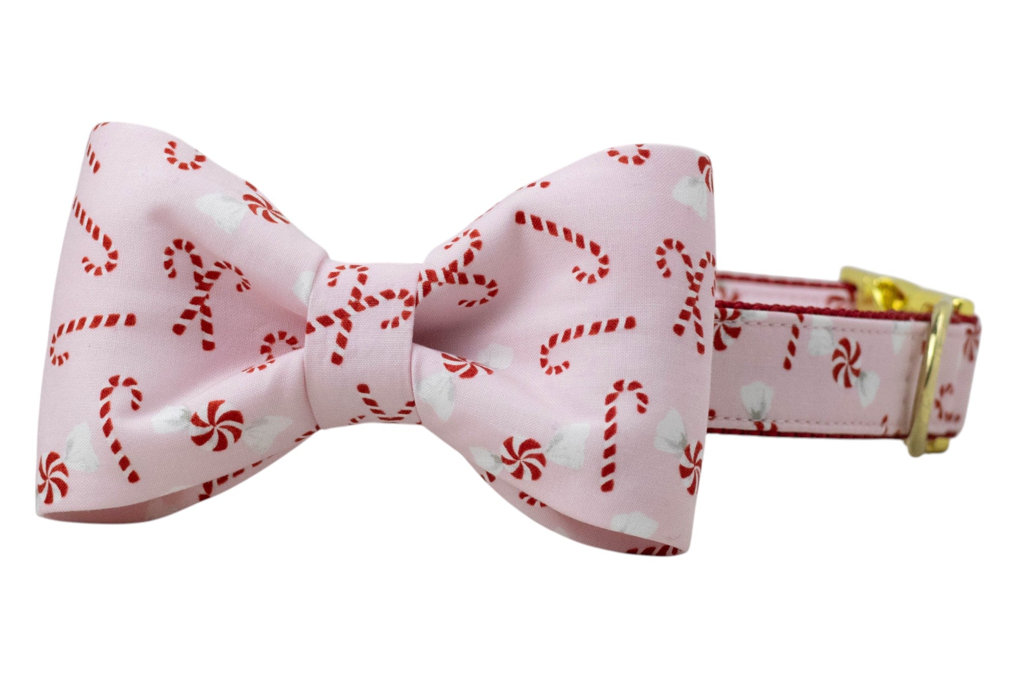A festive dog collar with an attached bow tie, both made from light pink fabric featuring candy canes and peppermint swirl candies. The bow tie is neatly structured and centered, while the collar includes a nylon backing and polished  hardware, including a D-ring and adjustable side-release buckle.