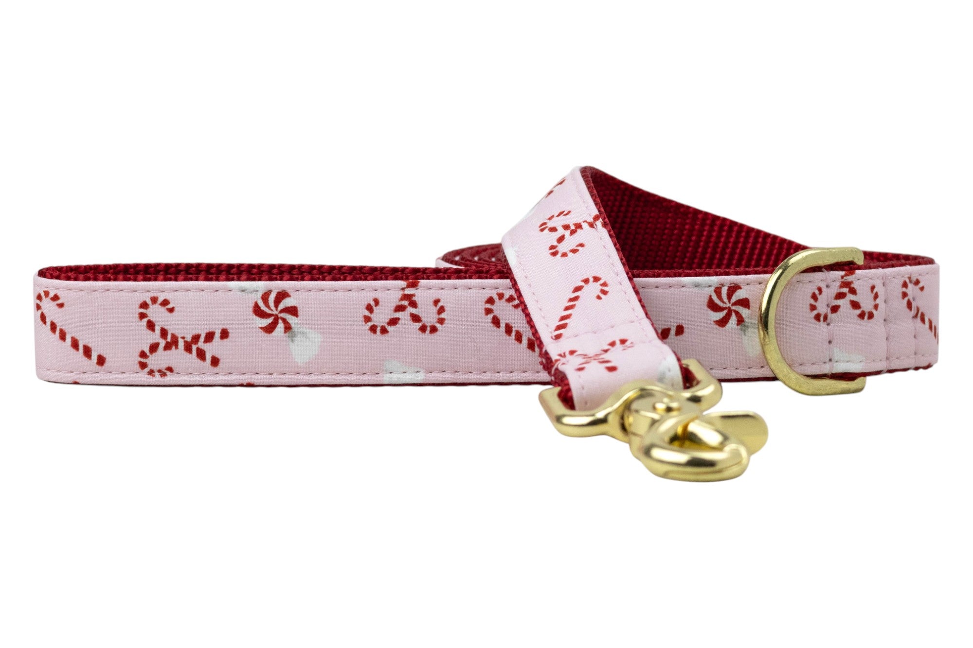 Holiday dog leash made from soft pink fabric decorated with striped candy canes and peppermint swirls. The leash is backed with vibrant nylon webbing and features metal hardware: a rotating leash clasp and an accessory D-ring near the looped handle.