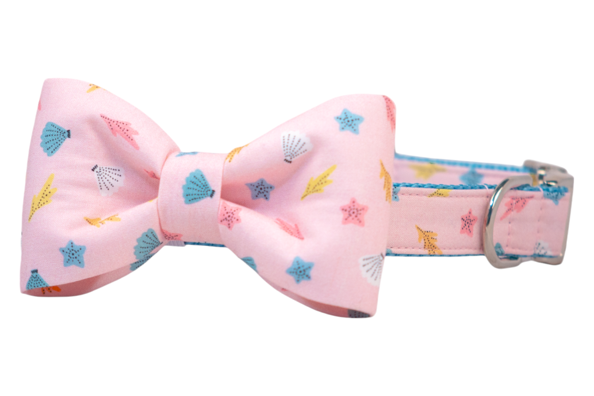 A soft pink dog collar with a matching oversized dog bowtie, both printed with an ocean-inspired pattern featuring blue starfish, scallop shells, pink coral, and yellow seaweed. The bow is neatly tied with rounded loops, and the collar includes a silver metal D-ring.