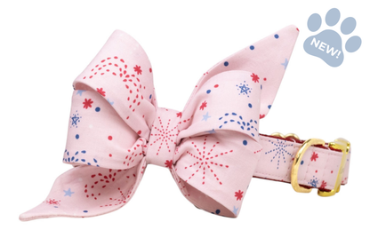 Soft pink collar with an oversized bow, printed with red and blue firework bursts and dots, paired with a gold-tone buckle.