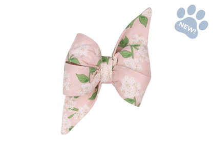 Hydrangea-print belle bow dog collar accessory featuring an oversized blush pink bow adorned with white hydrangea blooms and green leaves, finished with elegant pointed tails.