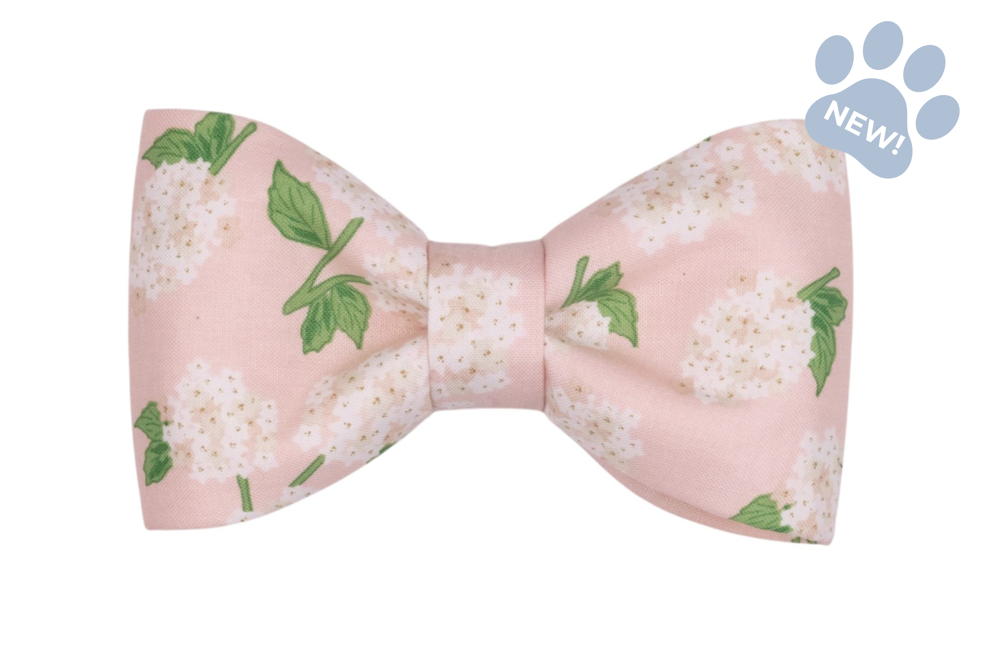 Hydrangea-print dog bow tie featuring a soft blush pink background with white hydrangea blooms and green leaves, styled in a classic bow shape.