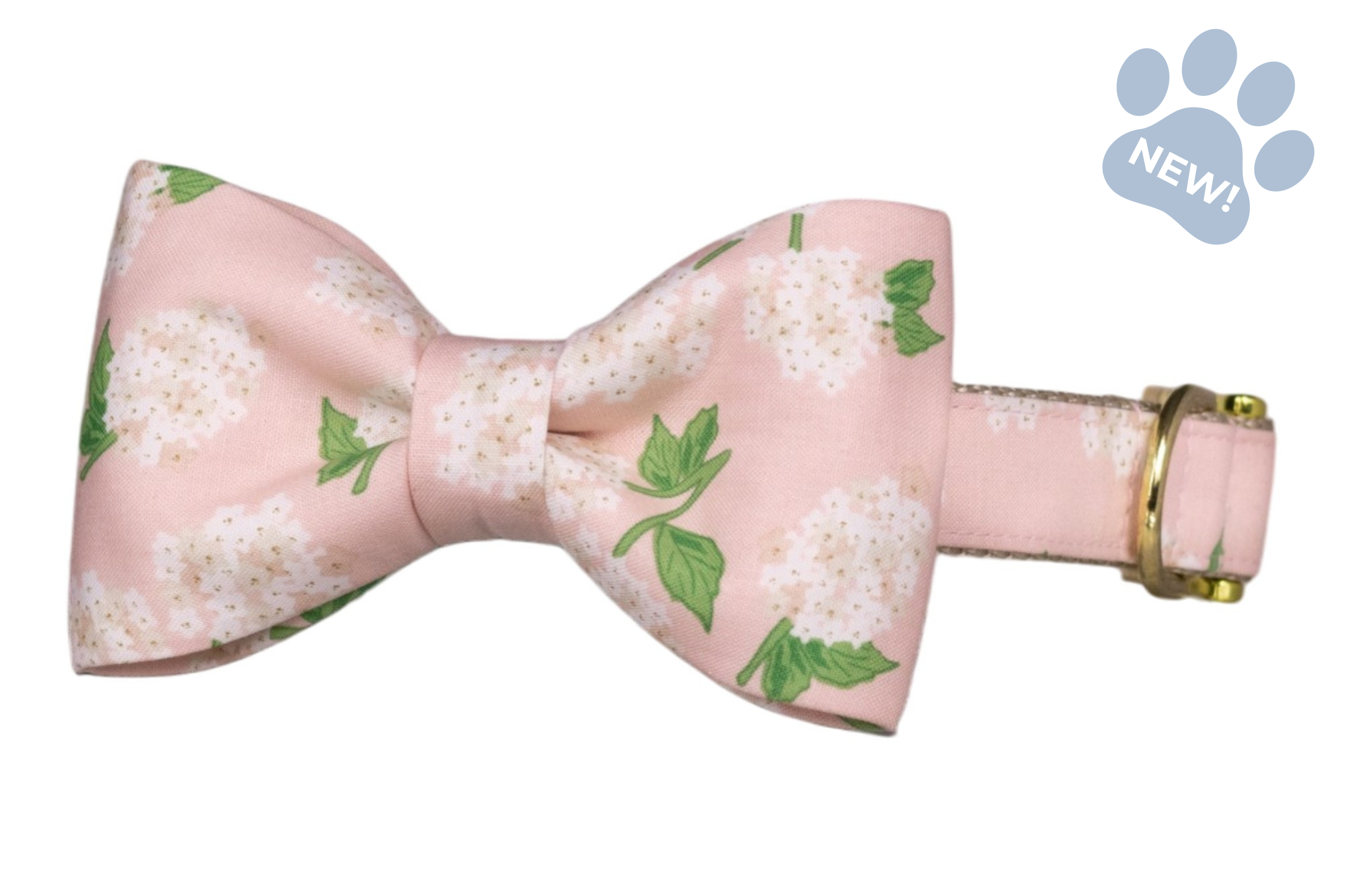 Hydrangea-print bow tie dog collar featuring a classic bow tie with white hydrangea blooms and green leaves on a blush pink background, attached to a matching collar with gold-tone hardware.