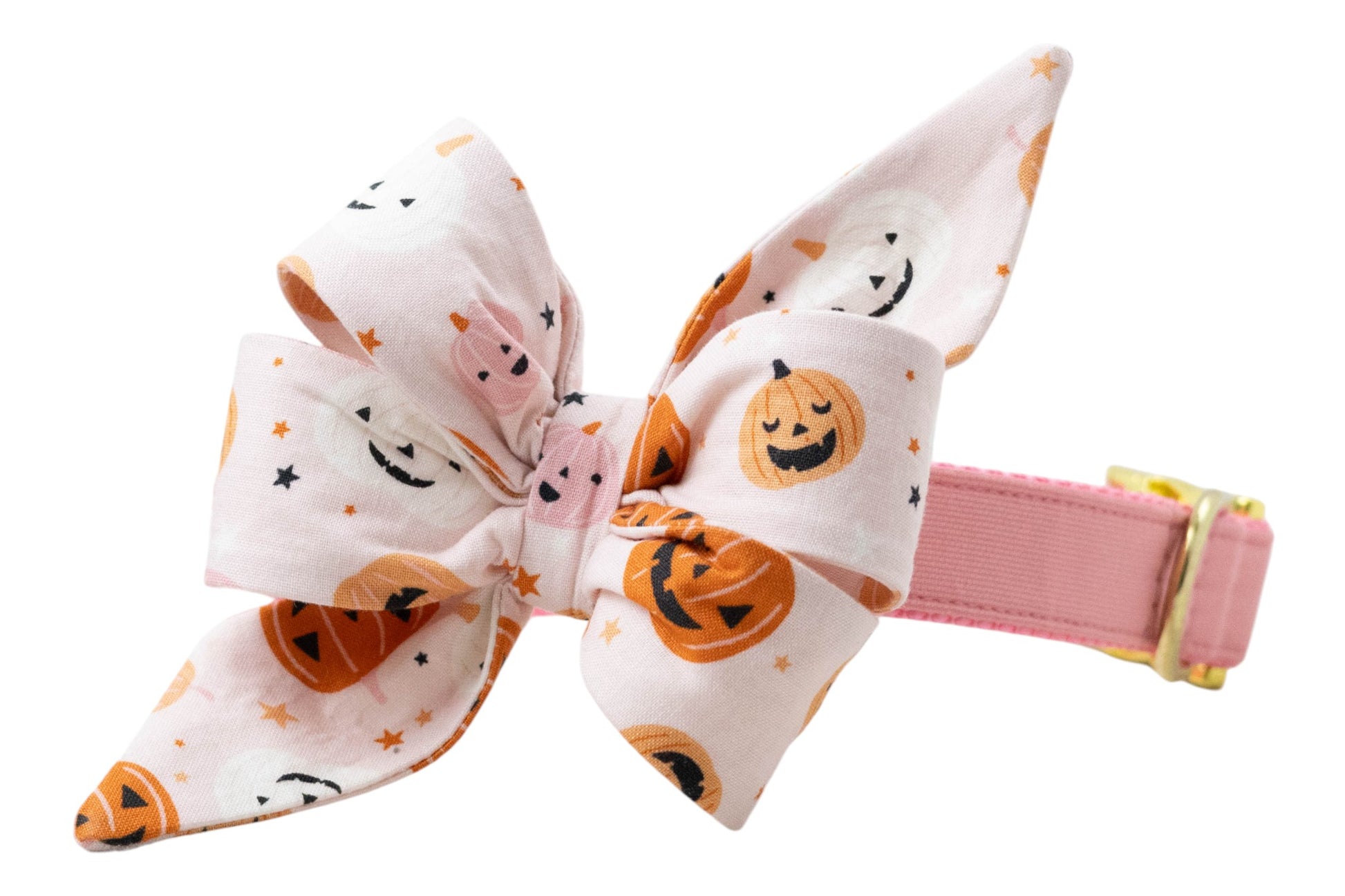 A soft pink dog collar with polished metal buckle accents and an attached large Halloween-themed belle bow. The bow features cartoon-style pumpkins with carved faces, plus tiny stars sprinkled throughout. The festive design combines playful charm with holiday spirit.