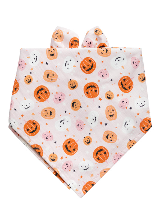 Halloween-themed dog bandana in a soft pink tone, folded into a triangle. The fabric is covered in a repeating print of smiling and spooky jack-o’-lantern faces, with assorted facial expressions, adding a whimsical and playful touch.