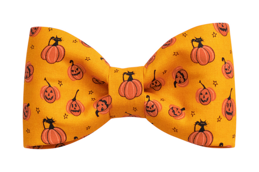 Halloween-themed do accessory: an orange bow tie printed with smiling jack-o'-lanterns, cat silhouettes, and small stars.