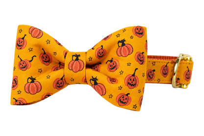 Classic dog collar featuring a Pumpkin Tails fabric bow tie, a golden orange fabric with small jack-o-lanterns and orange pumpkins, attached to a matching Pumpkin Tails collar with a nylon inner lining and gleaming gold hardware, including a D-ring and buckle.