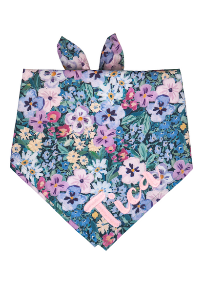 Colorful bandana for dogs adorned with a vibrant mix of hand-painted style pansy flowers, primarily in cool tones, and personalized with the name “Tica” in embroidered script.