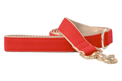A stylish red dog leash with beige backing and trim, finished with reinforced stitching and a polished gold-toned metal clasp and ring for durability and elegance.