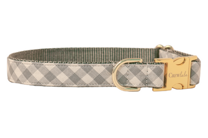 Stylish dog collar in pale gray gingham design, mounted on strong gray woven webbing for durability. The hardware includes a shiny clasp engraved with “Crewlala,” a robust D-ring for leash connection, and a metal sizing slider. Clean, even stitching outlines the collar, highlighting its neat, tailored construction.