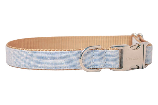 Light blue dog collar featuring a soft linen fabric with a subtle grid pattern, stitched onto nylon webbing. The collar includes a silver-tone metal D-ring and a polished side-release buckle engraved with the brand name “Crewlala.”