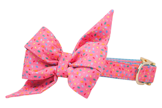 Playful dog collar with a vibrant sprinkle-print fabric in pink, decorated with a voluminous feminine belle bow. The belle bow’s exaggerated shape adds flair, and the collar is secured with a polished buckle and D-ring.