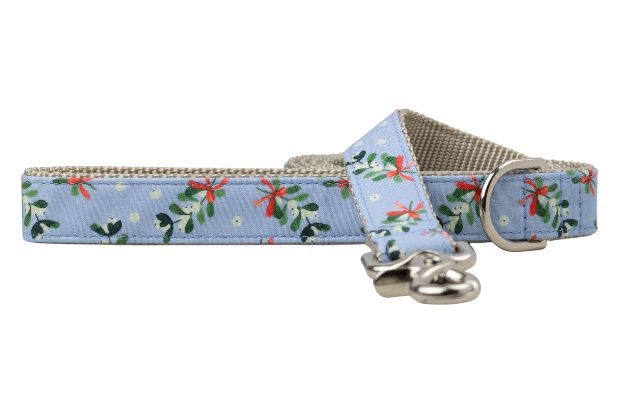 Winter-themed dog leash made from soft blue fabric decorated with mistletoe clusters tied with bows and surrounded by snow-like dots. The underside features nylon webbing for strength, and the leash includes hardware: a rotating clasp and D-ring for attaching accessories.