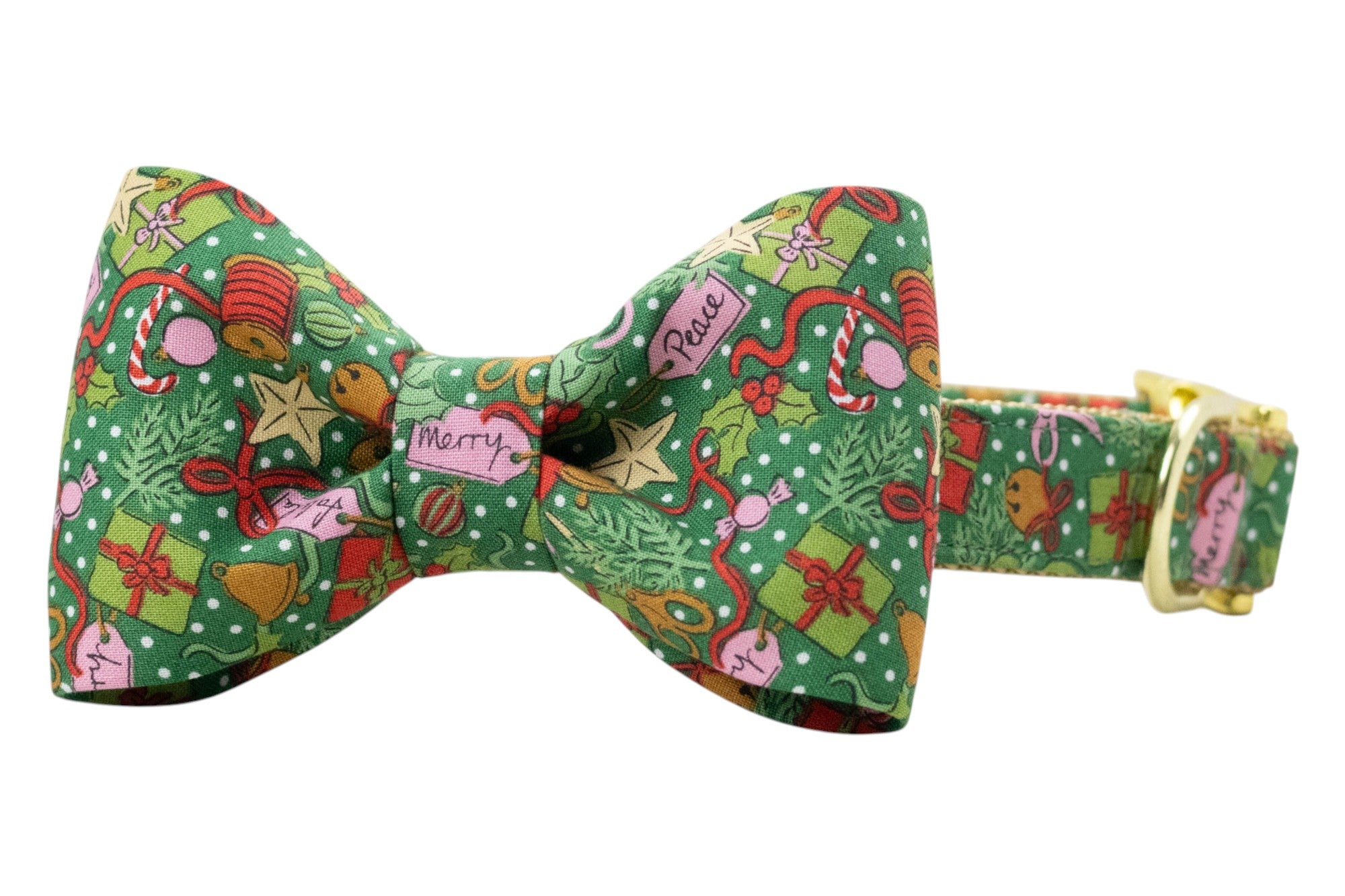 Green dog collar with an attached matching bow tie, made from fabric printed with festive Christmas designs including wrapped presents, holly sprigs, candy canes, bells, stars, ornaments, ribbon spools, and tags labeled “Merry” and “Peace,” all scattered over a background with snow-like dots. Collar features polished hardware, including a side-release buckle and D-ring.