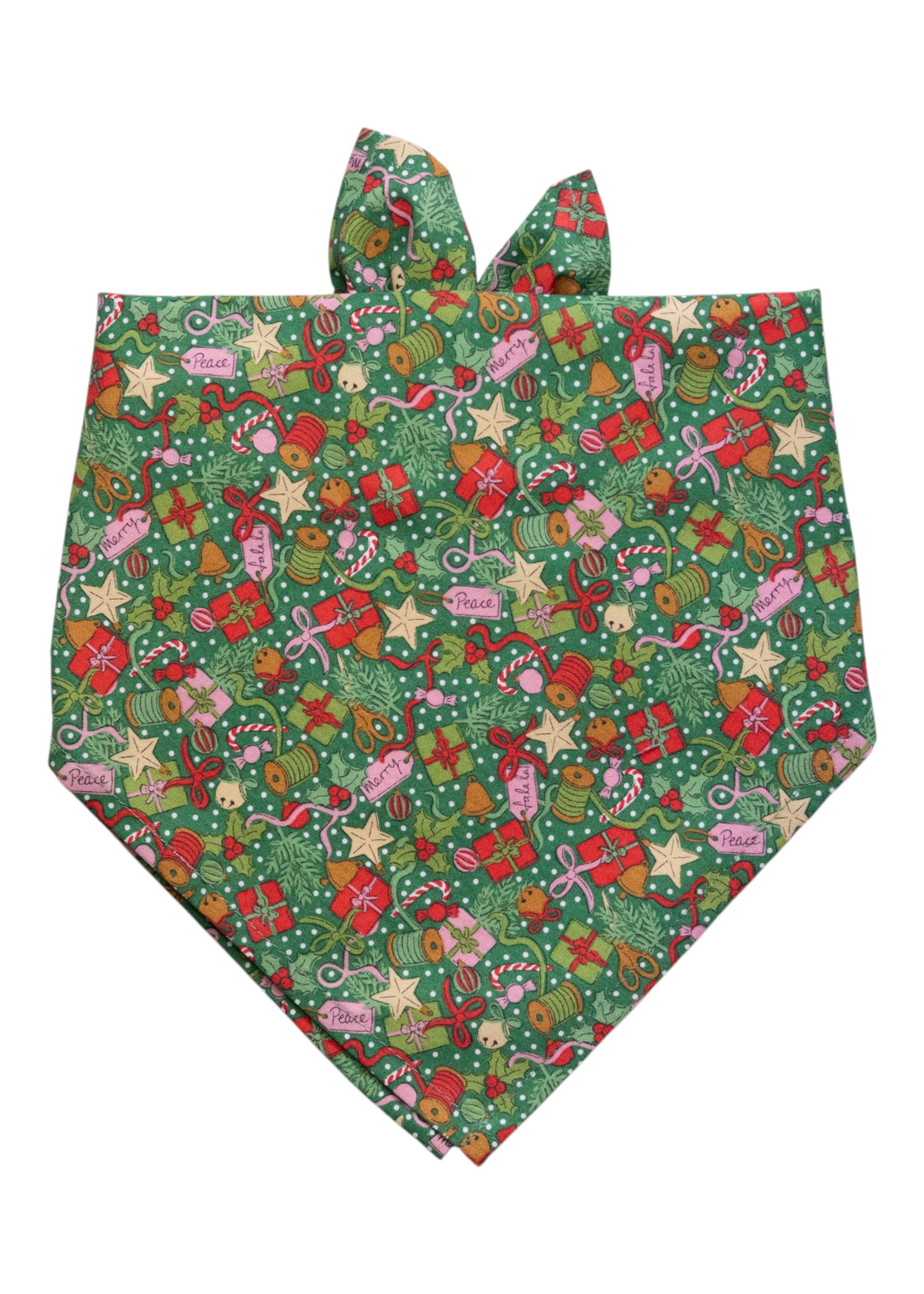Christmas-themed dog bandana with a green snowy background and a busy pattern of wrapped presents, stars, candy canes, holly, ornaments, spools of ribbon, and gift tags reading “Peace” and “Merry.”