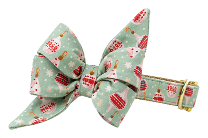 Dog collar featuring a large belle bow in Tinsel Time fabric, a soft sage mint print with pink and red glass ornaments, attached to a matching Tinsel Time collar with a nylon inner lining and gleaming gold hardware, including a D-ring and buckle.