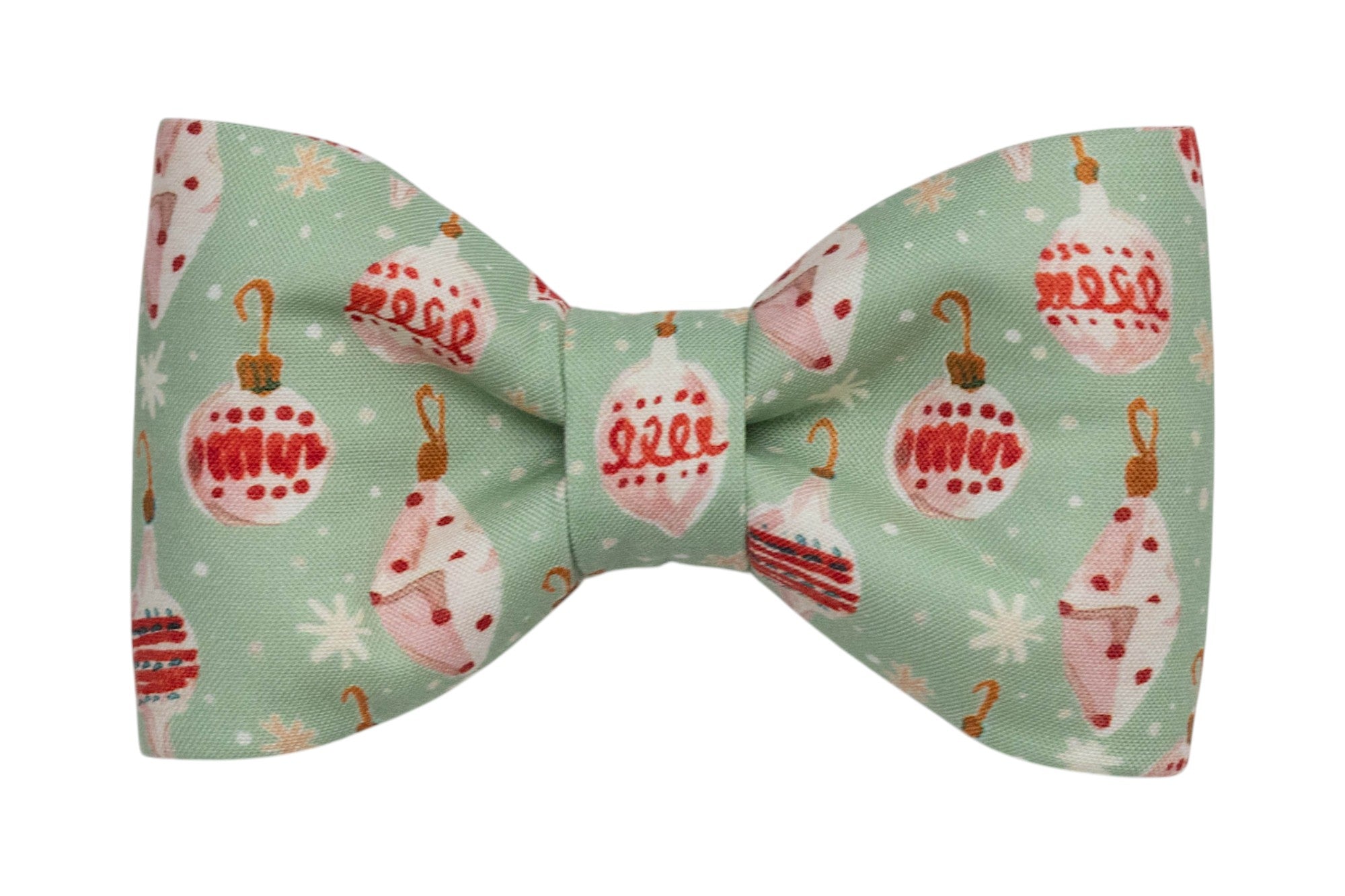 Holiday-themed dog bow tie in soft green fabric featuring illustrated Christmas baubles in festive colors, surrounded by snowflake and polka dot accents. The bow is centered and neatly cinched for a tidy, classic appearance, ideal for seasonal wear.