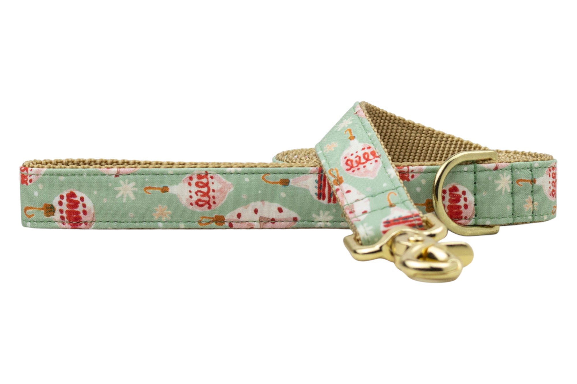A holiday dog leash featuring pale green fabric with vintage-style Christmas ornaments, hooks, and scattered white snowflakes. The leash has a woven nylon underside for durability and includes shiny  hardware, such as a swivel clasp and D-ring near the handle loop.