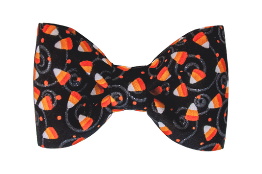 Halloween bow tie for dogs featuring a black fabric patterned with bright candy corn pieces. The design is accented with playful swirls and tiny dots, creating a fun, seasonal accessory for fall celebrations.