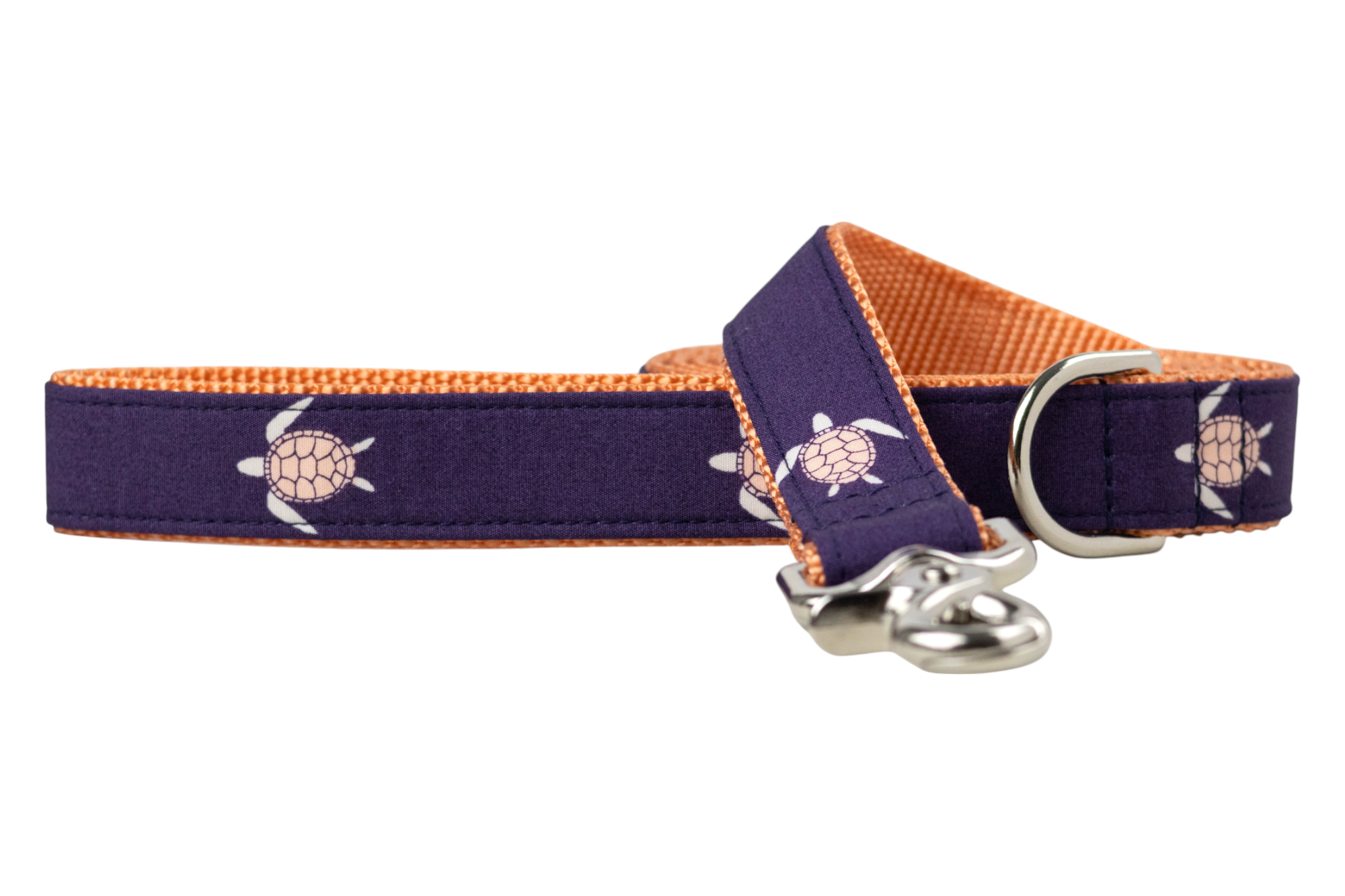 A dog leash with a dark purple fabric exterior featuring a repeating pattern of sea turtles with flippers and shell outlines. The interior is a bright orange woven material, and the leash is finished with a shiny silver clasp and a matching silver D-ring near the handle loop.