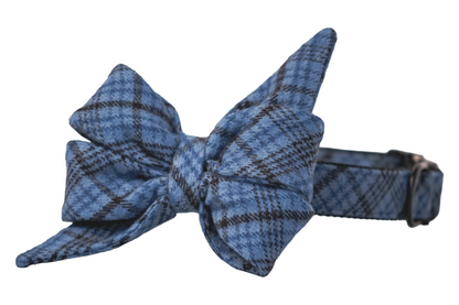 Blue flannel plaid dog collar with a large, structured belle bow attached in matching fabric. The collar has a buckle and hardware, complementing the plaid pattern, and is designed for both style and function.