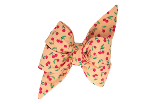 Add a touch of summer charm with this cherry-printed girl dog belle bow on a warm peach background.