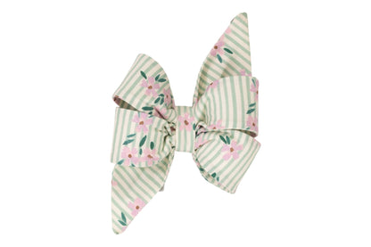 A decorative dog belle bow with long tails made of striped fabric in pale green and cream, featuring a pink floral pattern and green leaves.