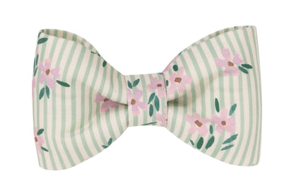 Close-up of a pastel-colored dog bow tie featuring soft green and cream stripes and small pink flowers with leafy accents.