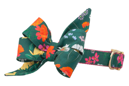 Statement dog collar with a large, feminine belle bow, made from dark green fabric decorated with multicolored flowers The collar includes a nylon webbing interior and shiny buckle and D-ring.