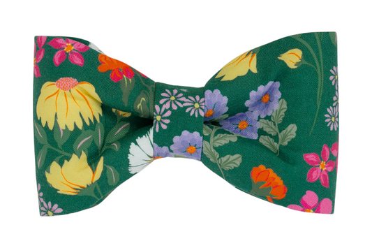 A handmade dog bow tie with a rich green backdrop, beautifully adorned with vibrant wildflowers in yellow, purple, pink, and white.