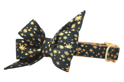 Dark green dog collar with an attached oversized belle bow featuring long, pointed ends. The fabric is decorated with metallic stars and starbursts in various sizes, giving it a festive, celestial look. The collar includes polished hardware and a nylon woven underside.