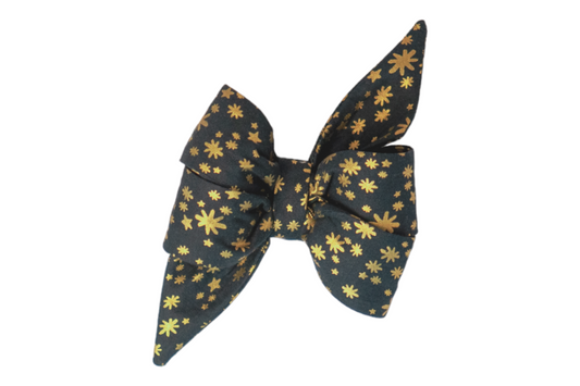 A festive dog belle bow with long, pointed tails made from dark green fabric, featuring a dazzling pattern of metallic stars and starbursts in varied sizes. The belle bow has a structured shape, with crisp edges and a central knot, giving it a feminine and elegant holiday appearance.