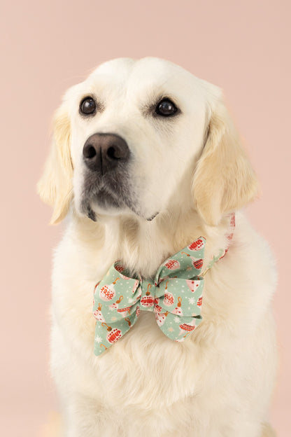Golden Retriever wearing a festive holiday belle bow dog collar with Christmas ornaments, posing against a soft background.