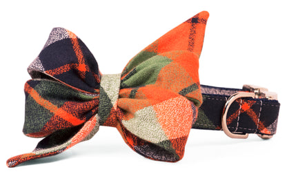 A flannel dog collar with a large belle bow in a fall-themed plaid pattern featuring warm fall colors. The collar includes polished hardware and stitching that matches the plaid design