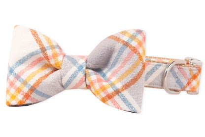 Plaid dog collar with a matching bow tie made from flannel fabric in warm and cool pastel tones. The bow tie is centered on the collar, which includes a D-ring for leash attachment.
