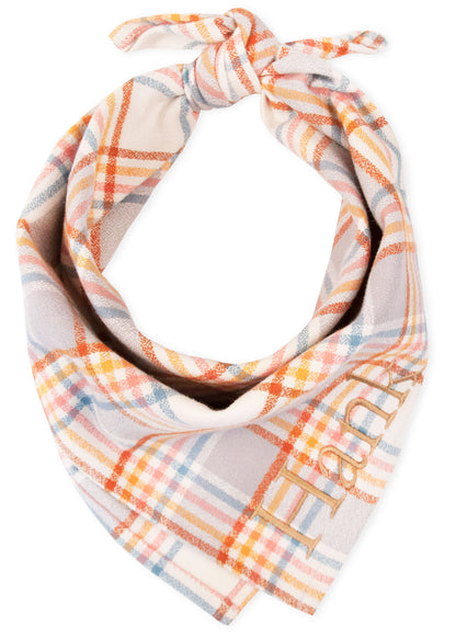 Close-up of a custom plaid dog bandana featuring soft flannel fabric with a light beige base and intersecting lines in warm and cool pastel shades. The bandana is tied into a knot and embroidered with the name “Hank” in tan-colored thread on one side.