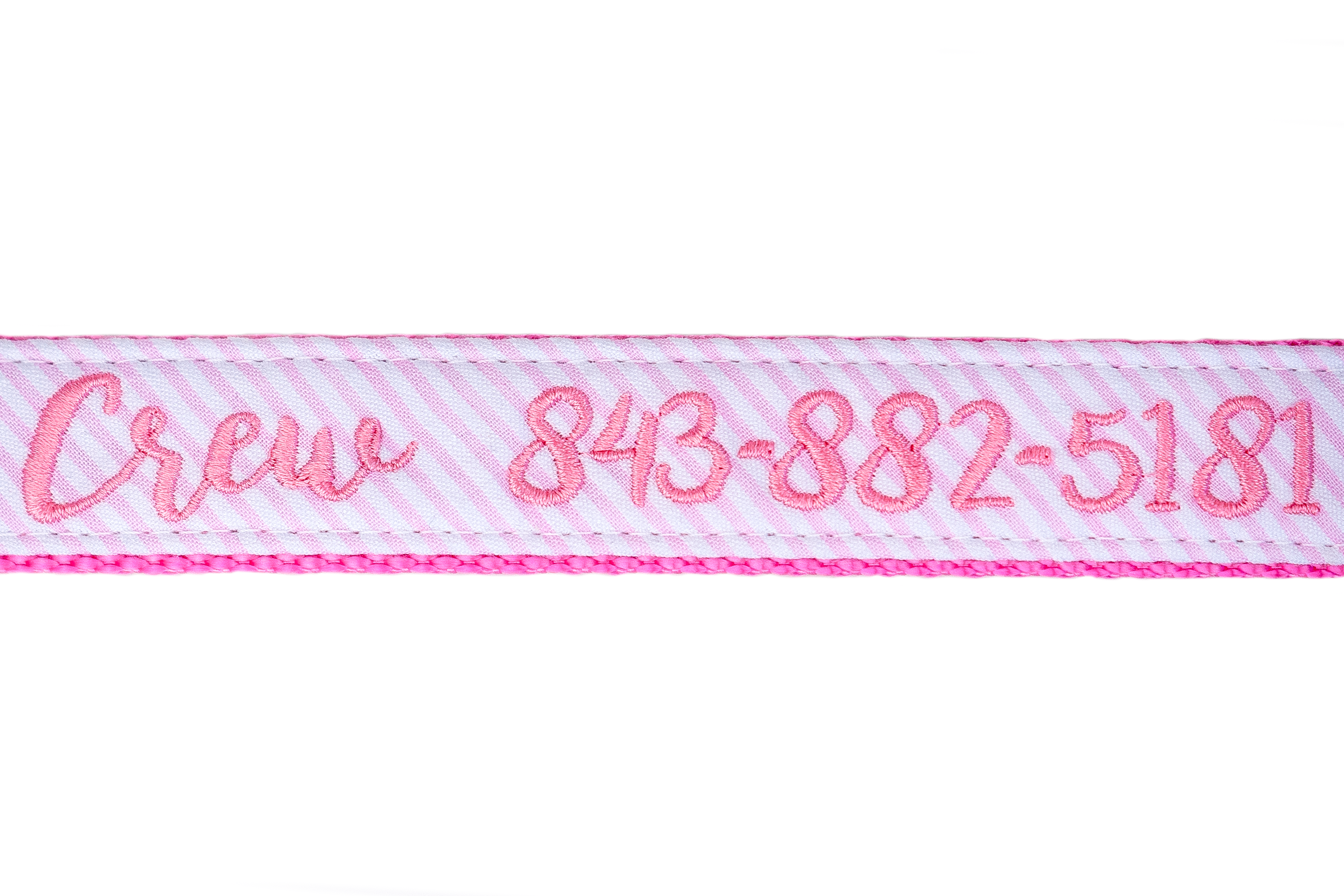 Close-up of a pink and white seersucker dog collar with bright pink embroidered text reading “Crew 843-882-5181.” The stitching is neatly sewn into the fabric, framed by hot pink webbing and double-stitched edges.