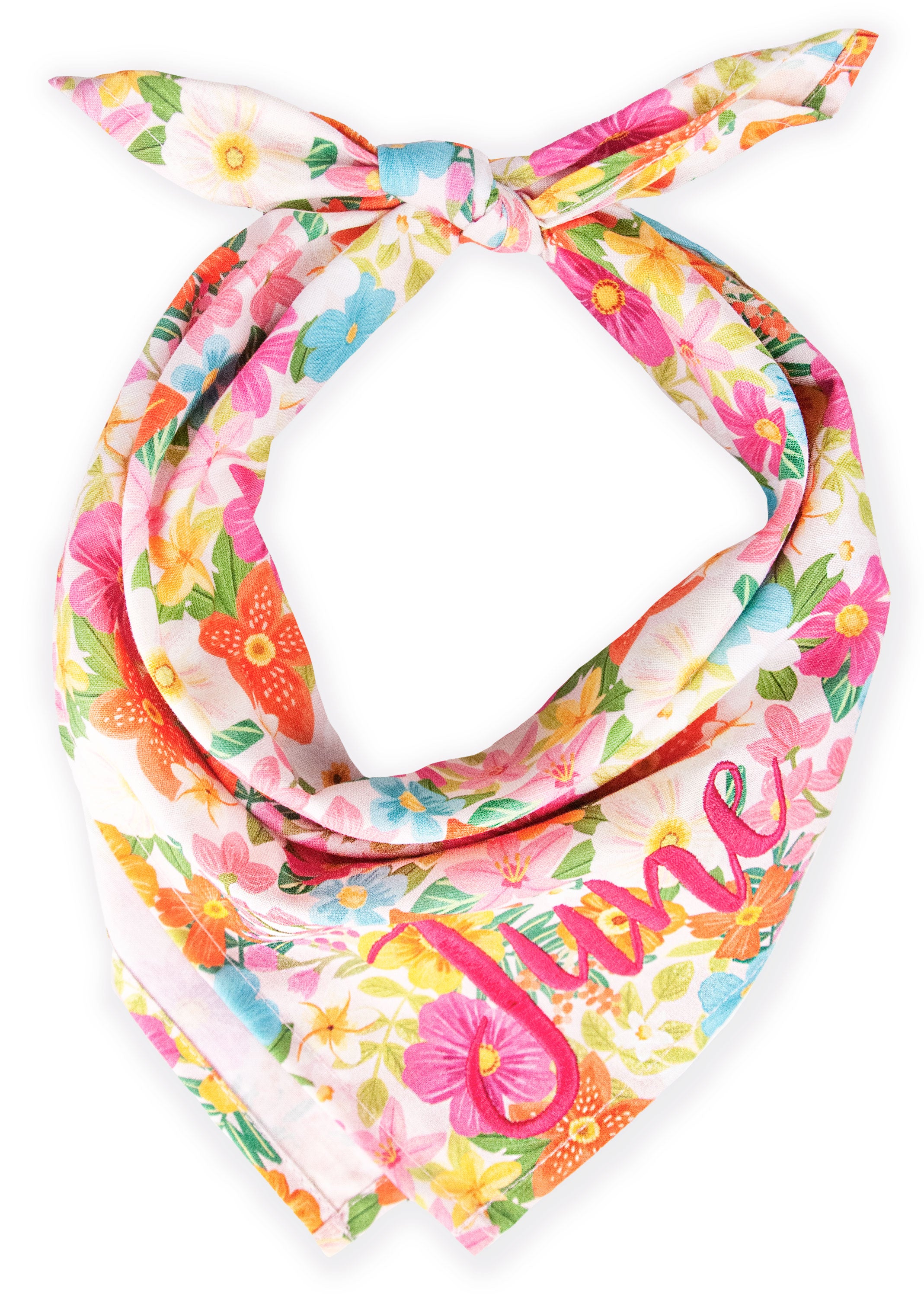 Custom floral dog bandana in a tie-on style, decorated with colorful tropical-inspired flowers and foliage. The design includes orange, pink, yellow, and blue blossoms scattered across a pale backdrop. The name “June” is stitched in vivid pink cursive near the pointed end of the bandana.