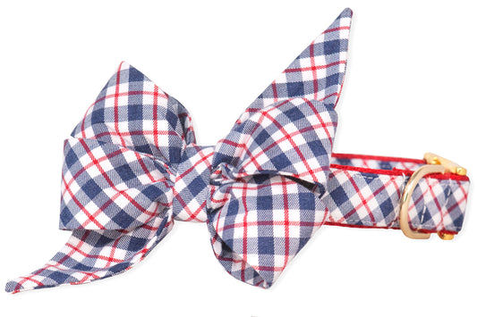 A decorative dog collar with a bold plaid bow tie in navy, red, and white. The feminine belle bow is voluminous and angular, adding a statement look to the matching collar, which is secured with a shiny gold-tone buckle.