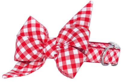Dog collar with a large red plaid feminine belle bow attached, designed with angular pointed ends and voluminous loops. The collar itself matches the belle bow’s fabric and is fastened with a polished metal buckle, blending classic style with playful detail.