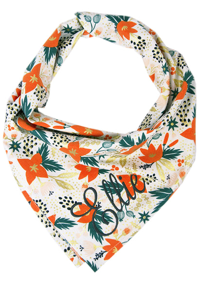 A festive dog bandana with a vibrant mix of orange florals, foliage, and metallic accents on a soft light background — the perfect seasonal accessory for stylish pups. The name "Ellie" is embroidered on the bottom right.
