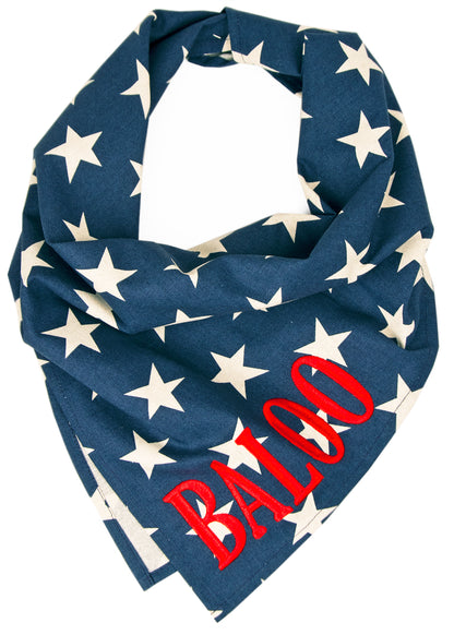 Personalized dog bandana featuring a dark blue background with scattered ivory stars and vivid red embroidered text reading “BALOO” on the lower corner. The bandana is styled in a folded triangle, perfect for festive or everyday wear.