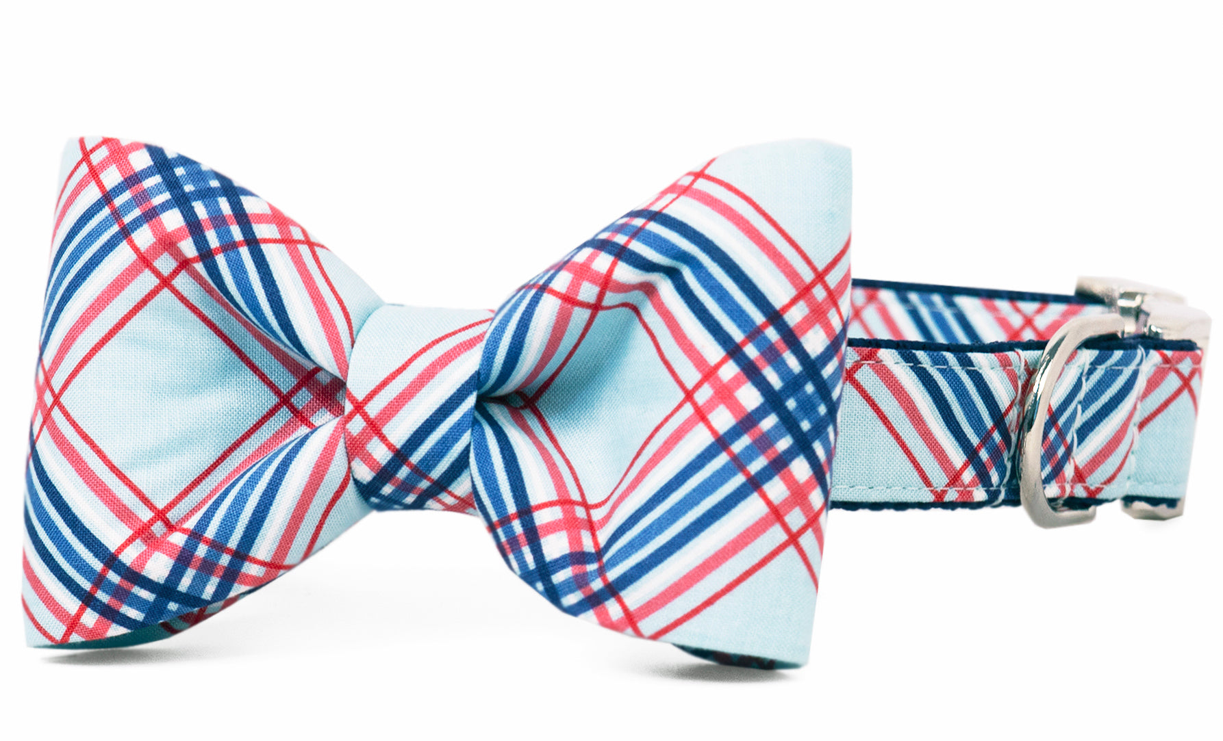 Close-up of a stylish dog collar featuring a large bow tie in a red, blue, and white plaid pattern. The collar matches the bow’s design and is finished with shiny silver hardware for secure fastening.