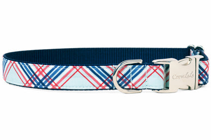 A dog collar with a red, white, and blue plaid pattern on a light blue background. The collar has a navy blue interior lining and is finished with silver hardware, including a D-ring and a side-release buckle engraved with the brand name "Crew LaLa."
